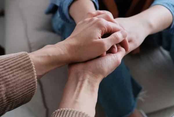 Two people holding hands on a couch, representing compassionate companioning and presence