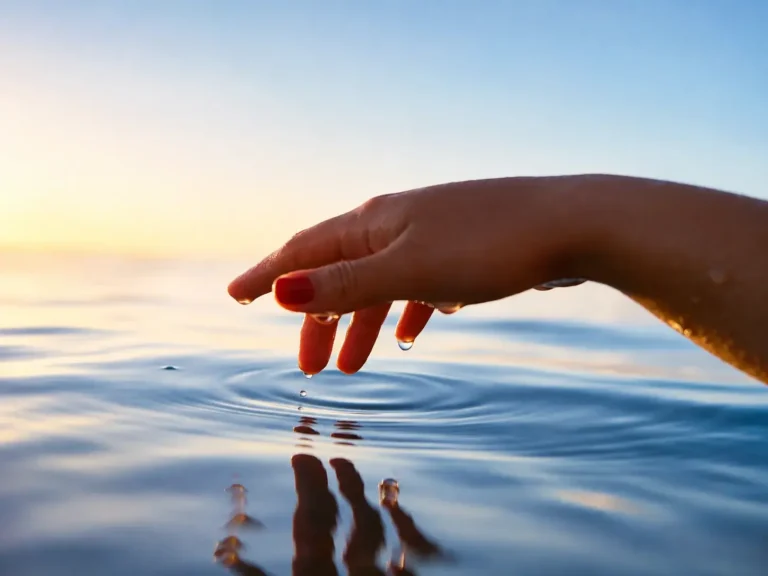 Hand touching still water at sunrise, ripples spreading outward