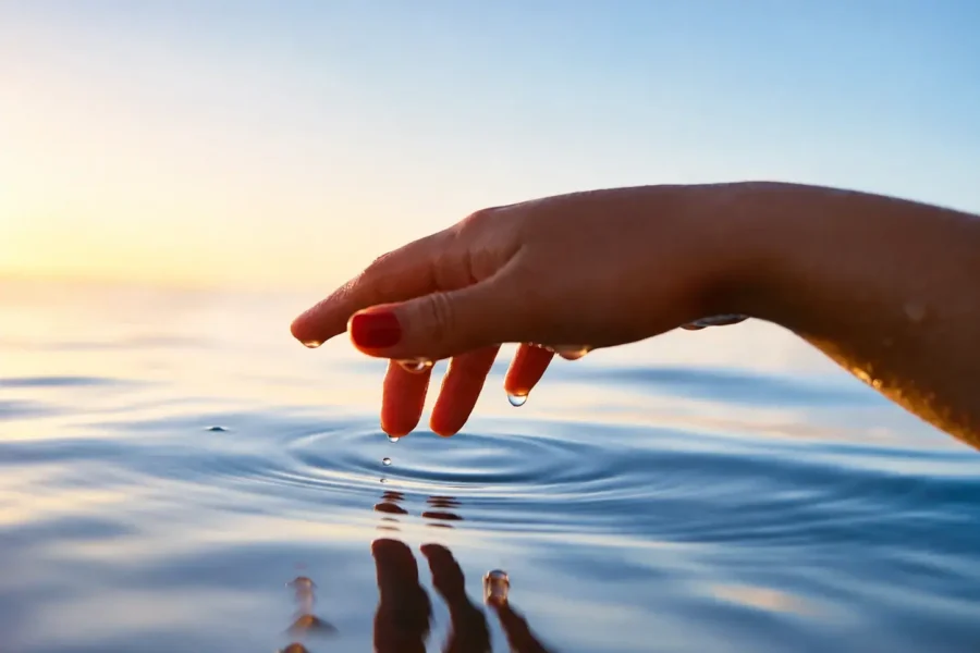 Hand touching still water at sunrise, ripples spreading outward