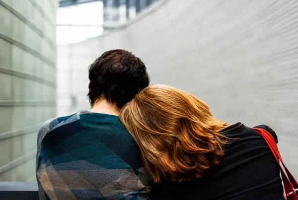 Two people sitting close together, one leaning on the other for support