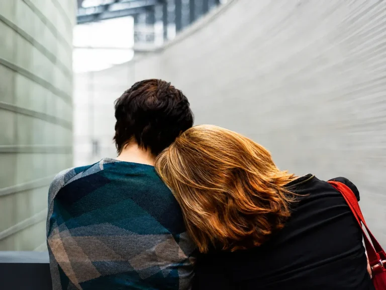 Two people sitting close together, one leaning on the other for support