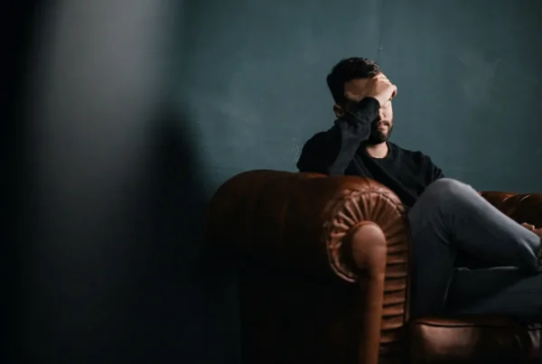 Man sitting alone on a sofa in low light, struggling with his mental health
