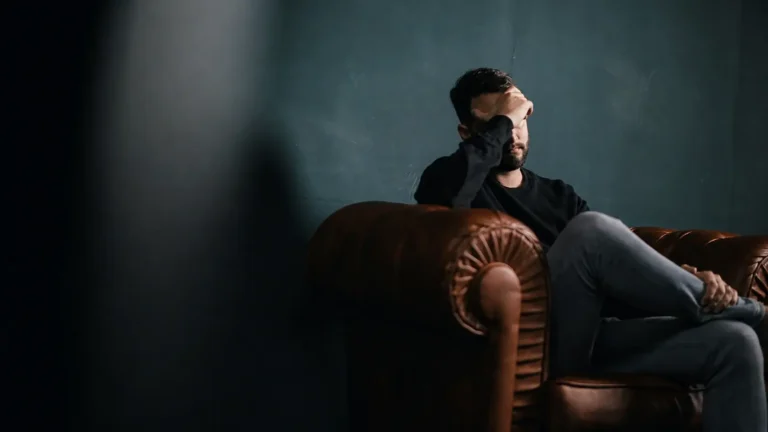 Man sitting alone on a sofa in low light, struggling with his mental health